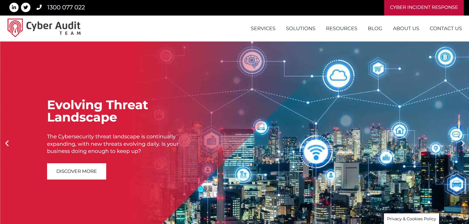 Alt text: Cyber Audit Team cybersecurity website homepage featuring a red and blue cityscape background with digital network icons, headline “Evolving Threat Landscape,” and a “Discover More” button.